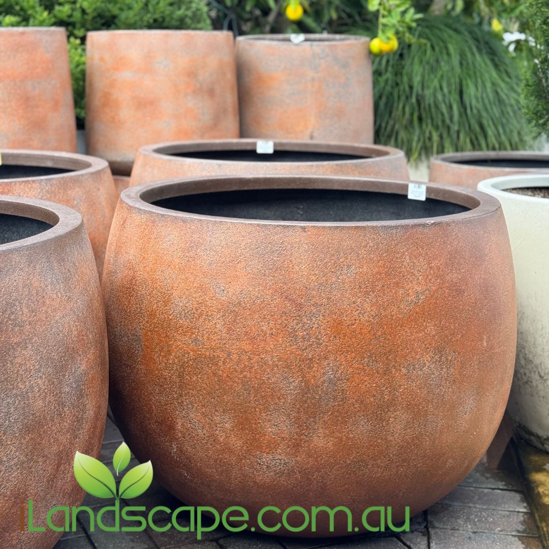 A collection of cylindrical concrete planters in various sizes with a textured, terrazzo-like finish, displayed outdoors.