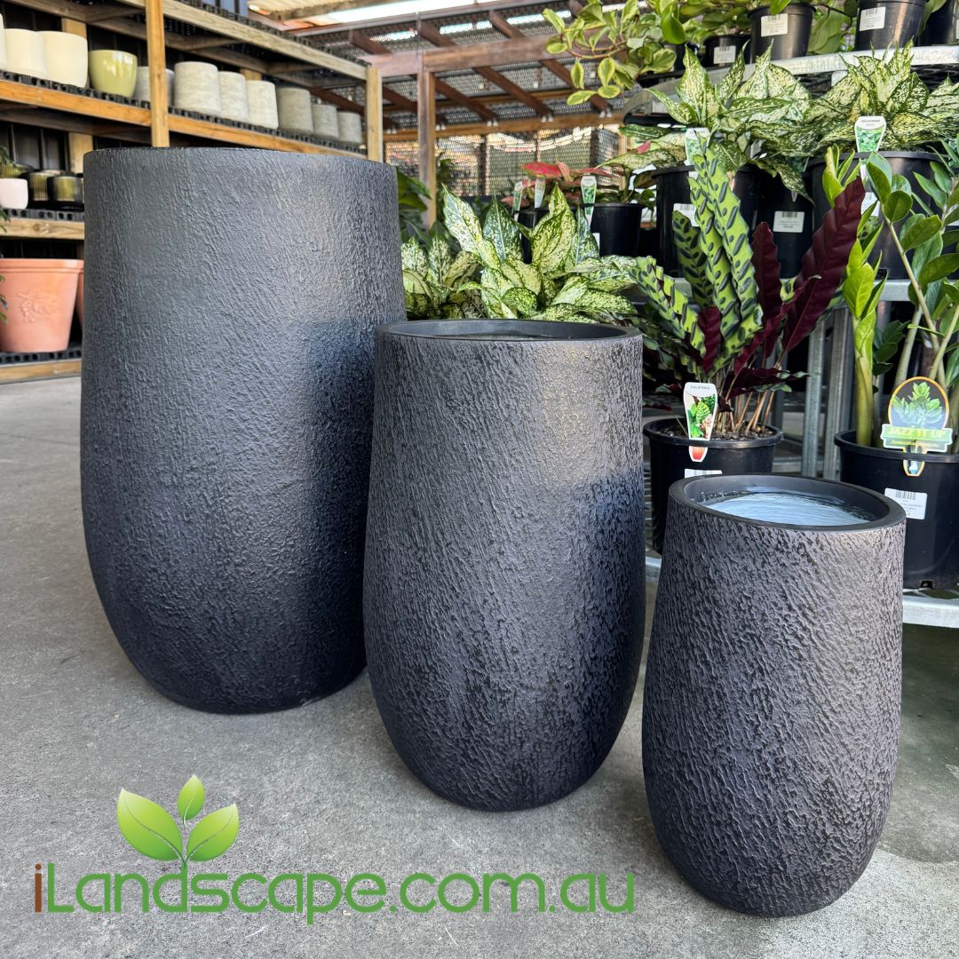 Three dark gray textured planters on a concrete floor with plants and shelves in the background, featuring the iLandscape.com.